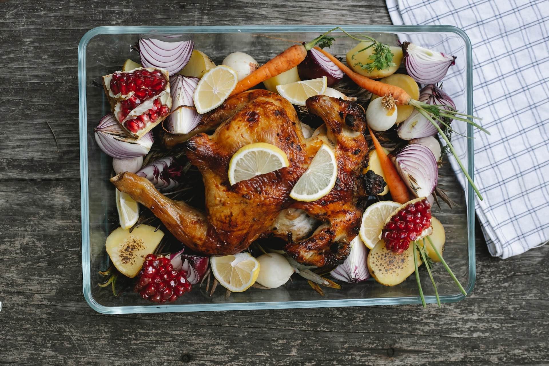 Ein Ofenblech mit einem schön gebratenen Hähnchen in der Mitte, umgeben von einer Reihe von gebratenem Gemüse, ist ein schnelles und preisgünstiges Gericht für stressige Abende