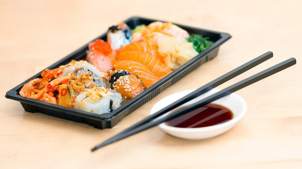 Ein verführerischer Behälter zum Mitnehmen, gefüllt mit einer Auswahl an Sushirollen und Sashimi.